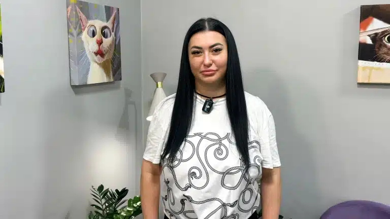 Чорнява дівчина в білій футболці стоїть біля картини з котиком