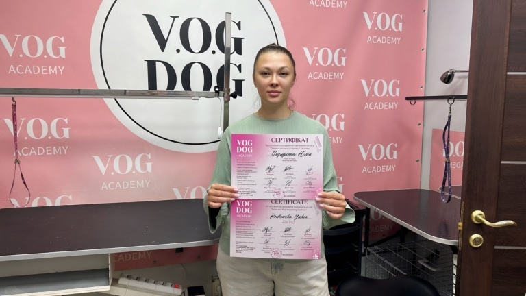 Дівчина з хвостиком та зеленій кофті тримає сертифікати біля грумерських столів