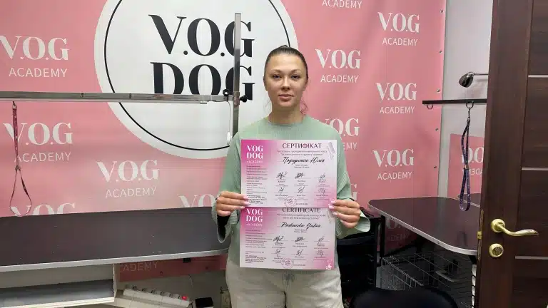 Дівчина з хвостиком та зеленій кофті тримає сертифікати біля грумерських столів