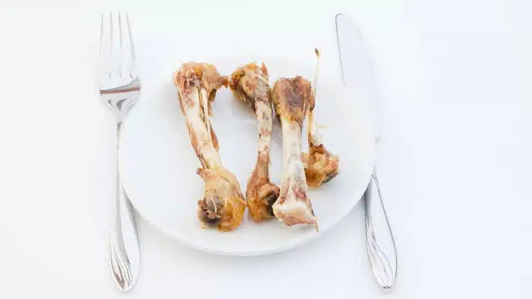 На білій тарілці лежать чотири кістки, а поруч - виделка та ніж