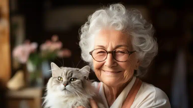 Приємна бабуся в круглих окулярах посміхається поруч з сірою кішкою