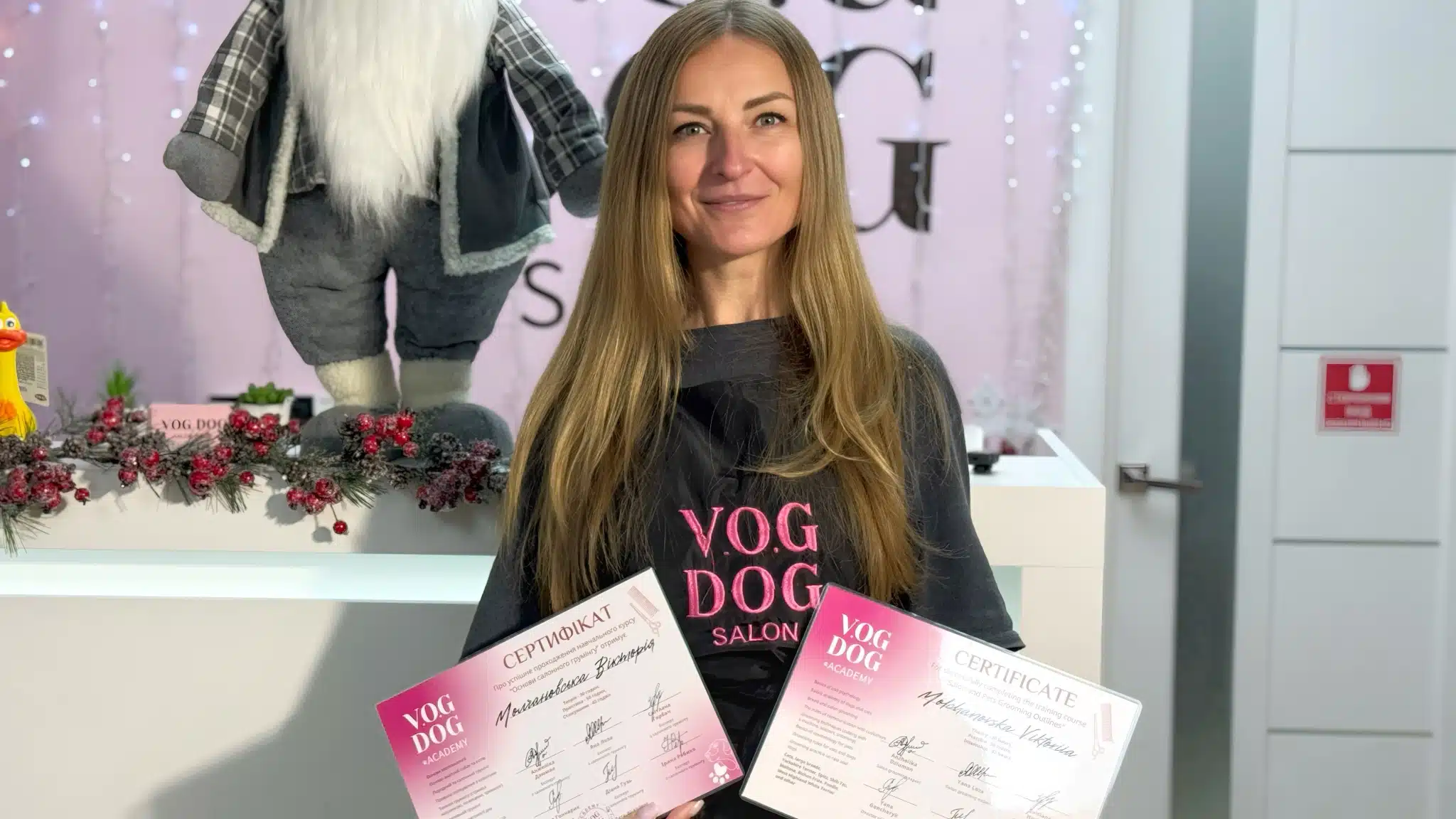 Дівчина з довгим волоссям демонструє отримані дипломи з курсів грумінгу