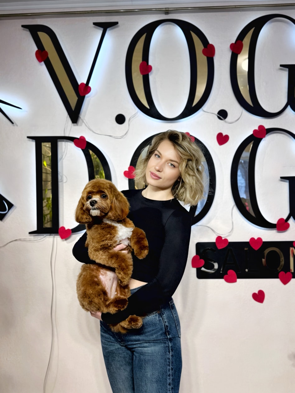 Дівчина в джинсах та чорному лонгсліві тримає коричневого мальтіпу