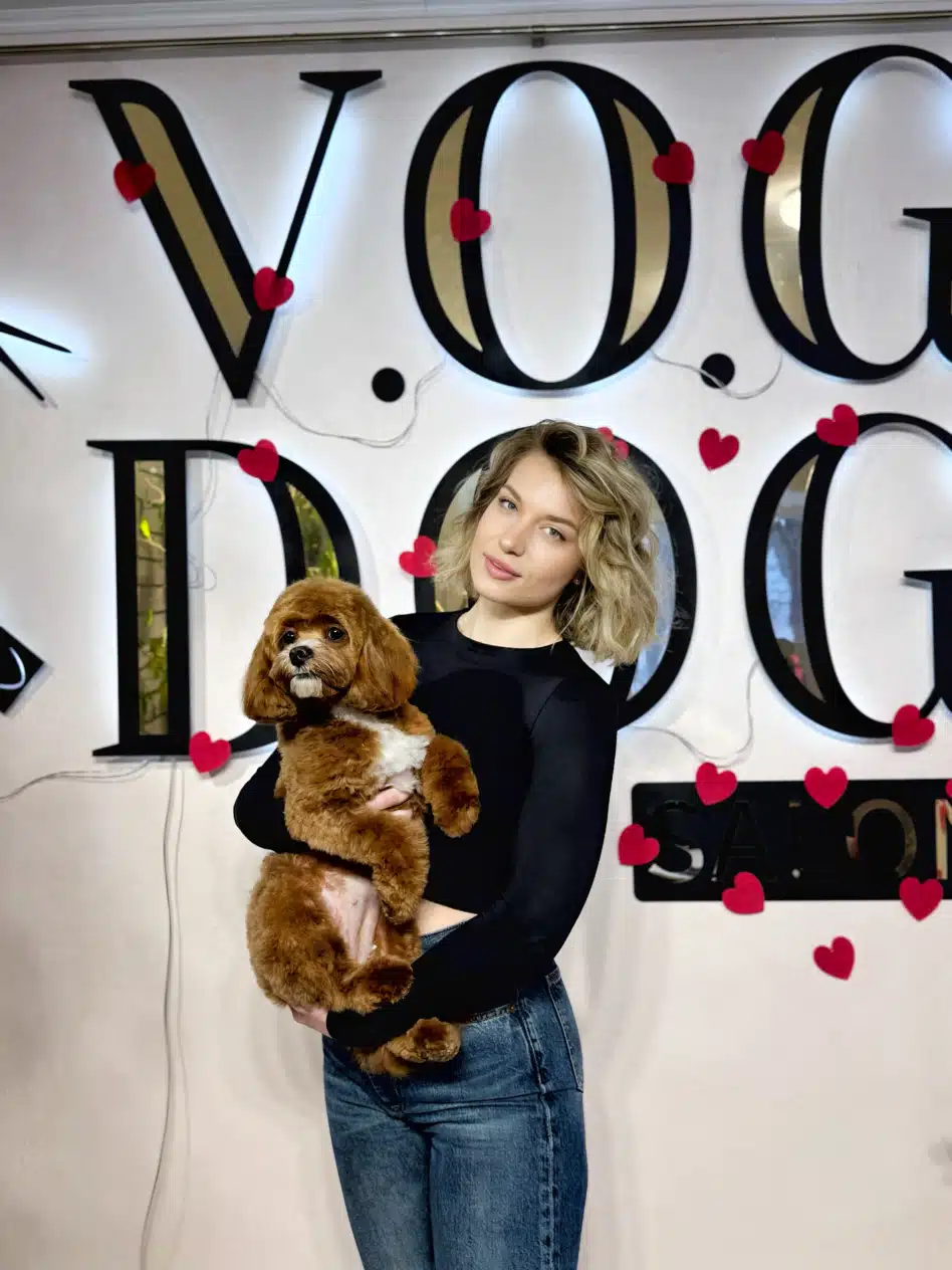 Дівчина в джинсах та чорному лонгсліві тримає коричневого мальтіпу