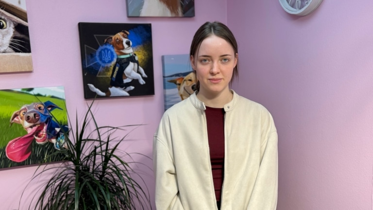 Дівчина в бордовій футболці та білій кофтинці уважно дивиться в камеру