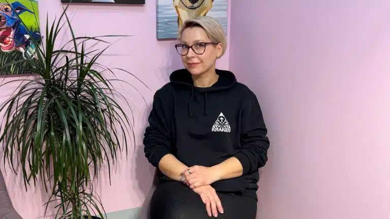 Дівчина з короткою стрижкою та чорними окулярами присіла біля вічнозеленої рослини