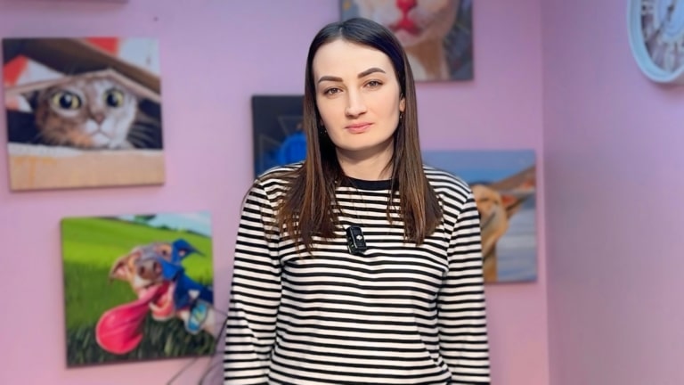 Дівчина в смугастому чорно-білому светрику стоїть поруч з круглим білим годинником