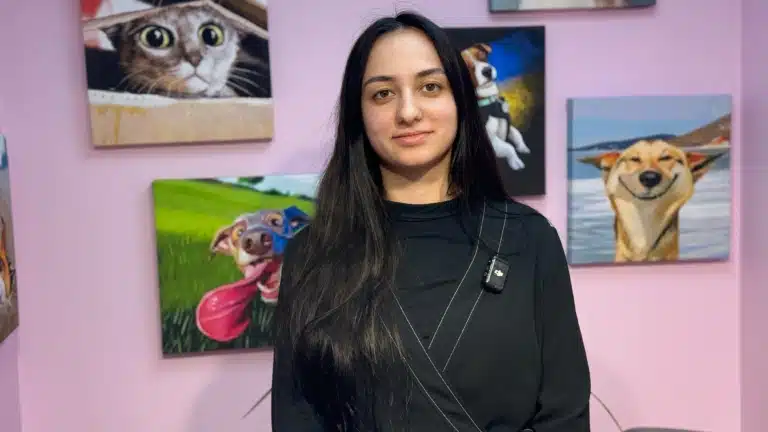 Дівчина з довгим чорним волоссям стоїть біля рожевої стіни з яскравими картинками