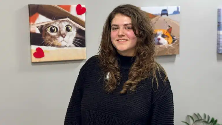 Кудрява дівчина у чорному светрі стоїть на фоні картин з тваринами