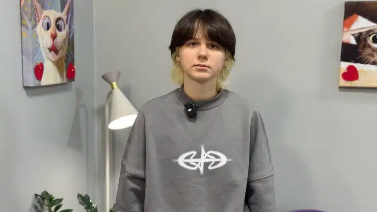 Дівчина з двоколірним фарбуванням та у сірому світшоті стоїть серед картин з тваринами