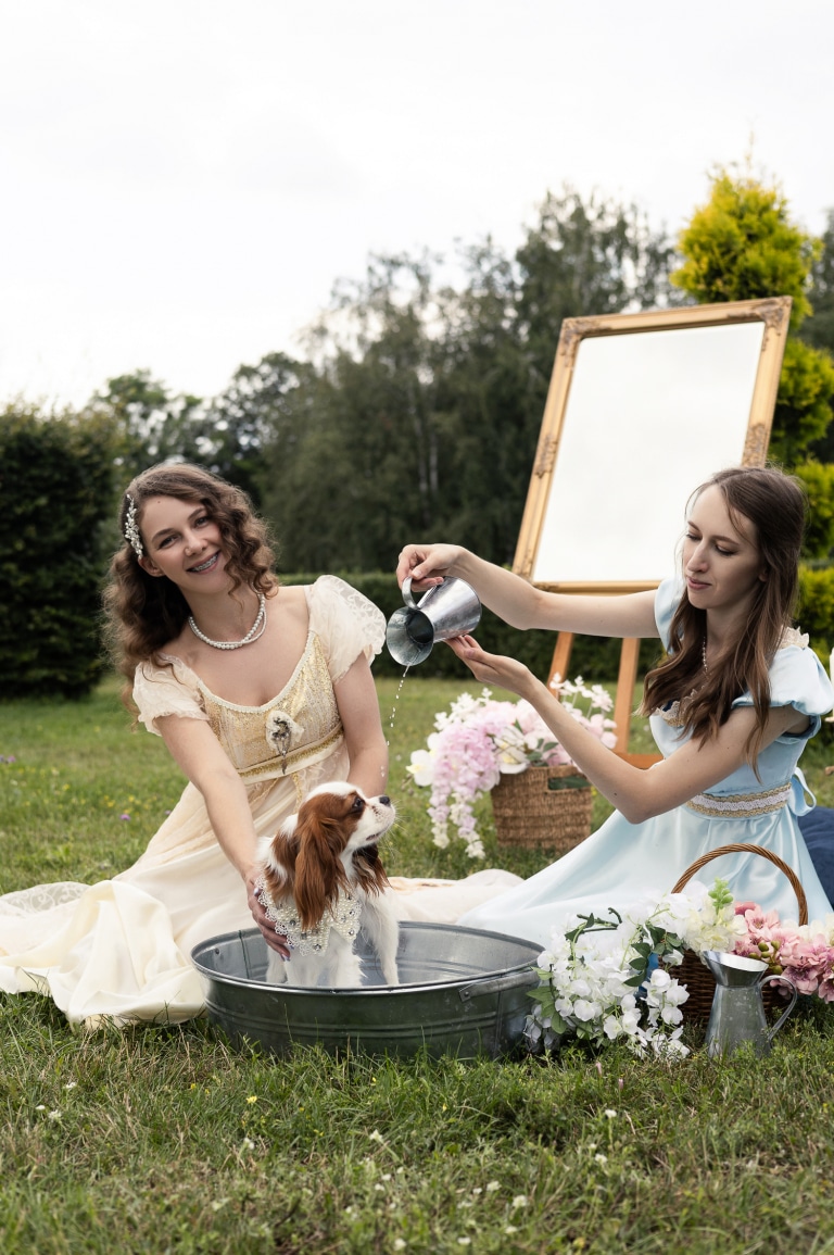Дівчина в блакитній сукні ллє воду на спину спанієля з глечика