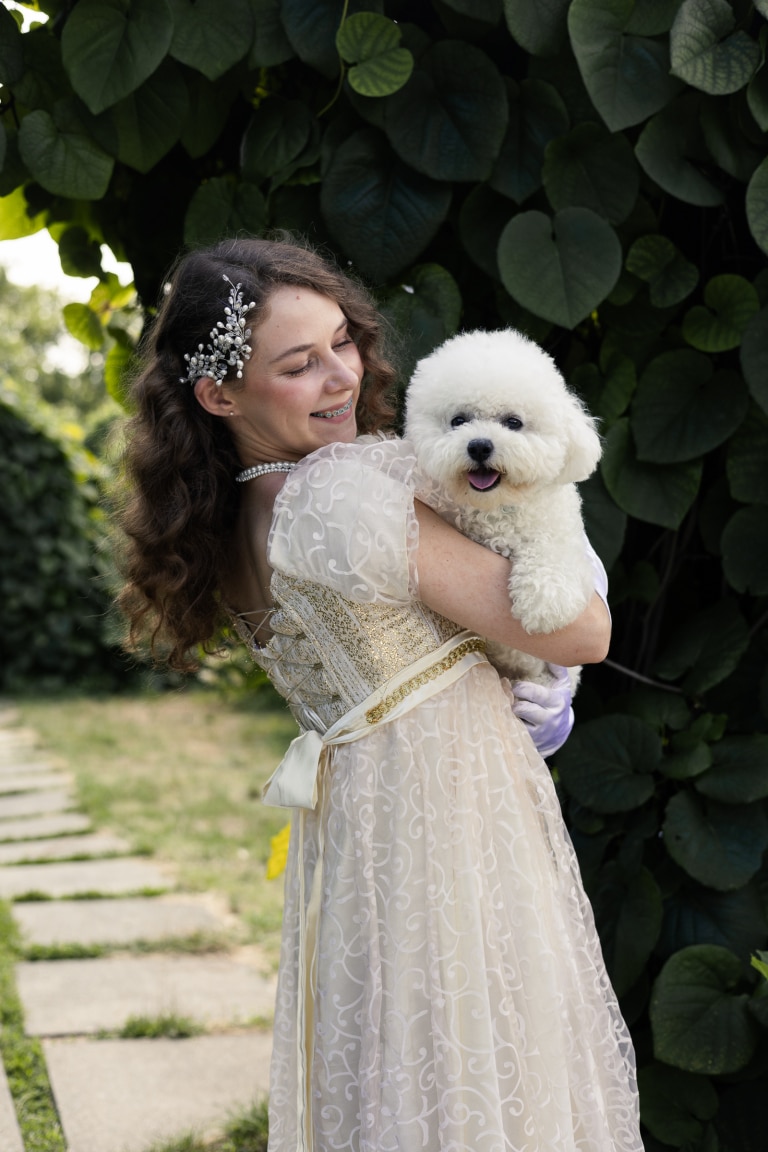 Дівчина в сукні кольору шампанського всміхається до бішона