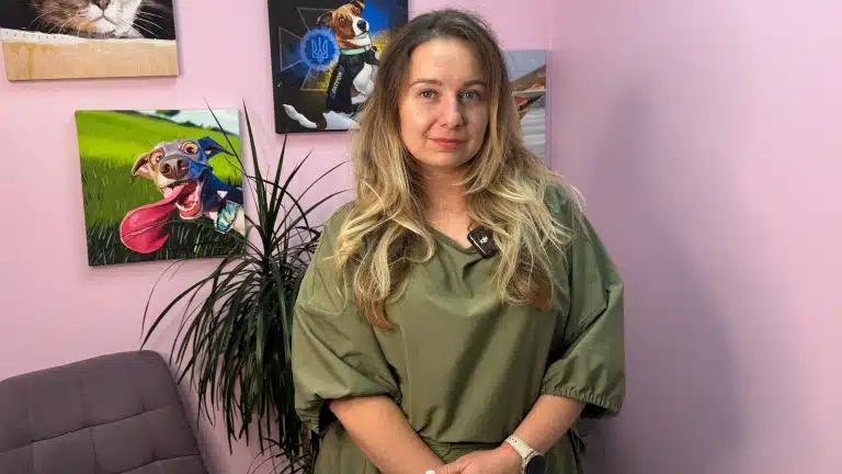 Жінка в зеленій сукні стоїть спиною до картин з зображенням тварин