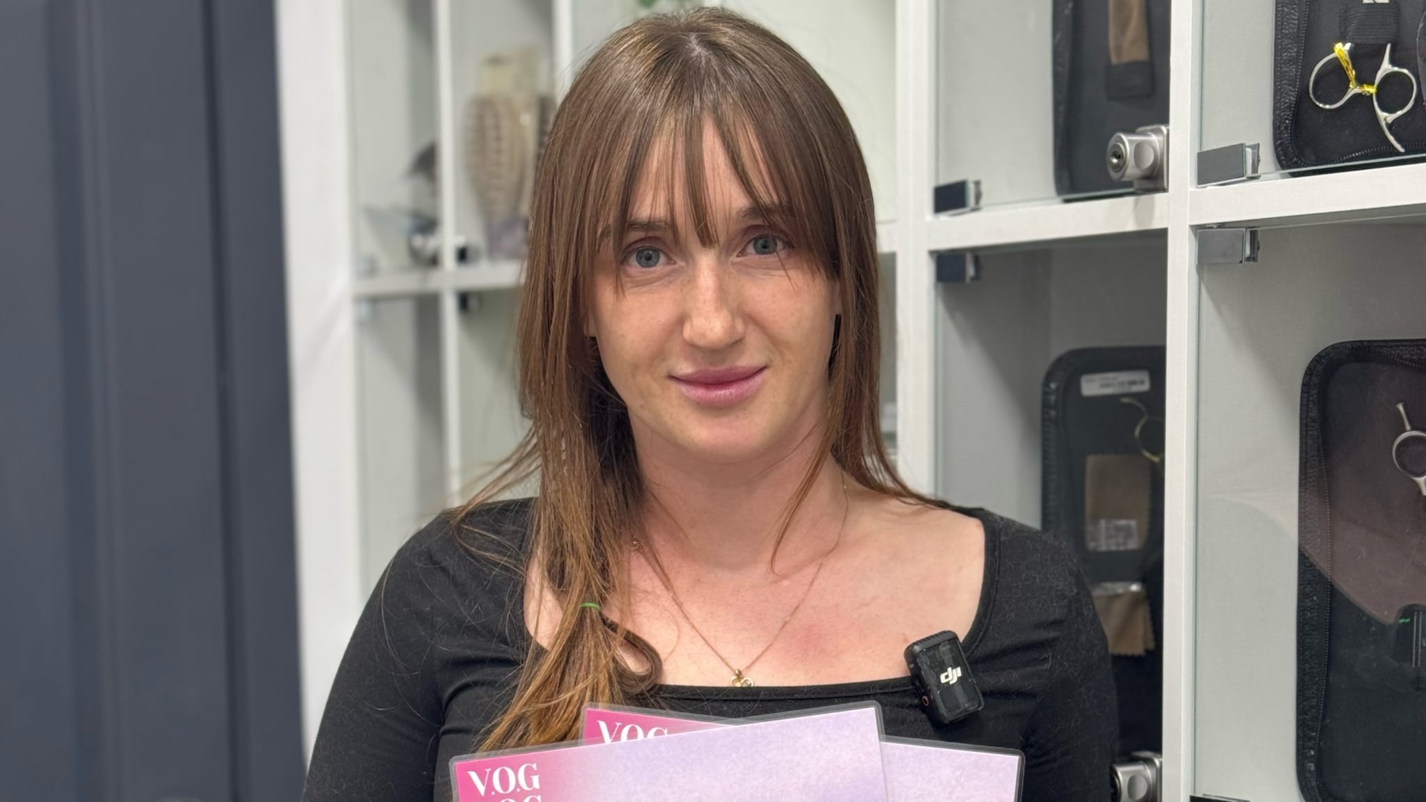 Дівчина з рівним волоссям та чубчиком тримає біля грудей рожеві сертифікати