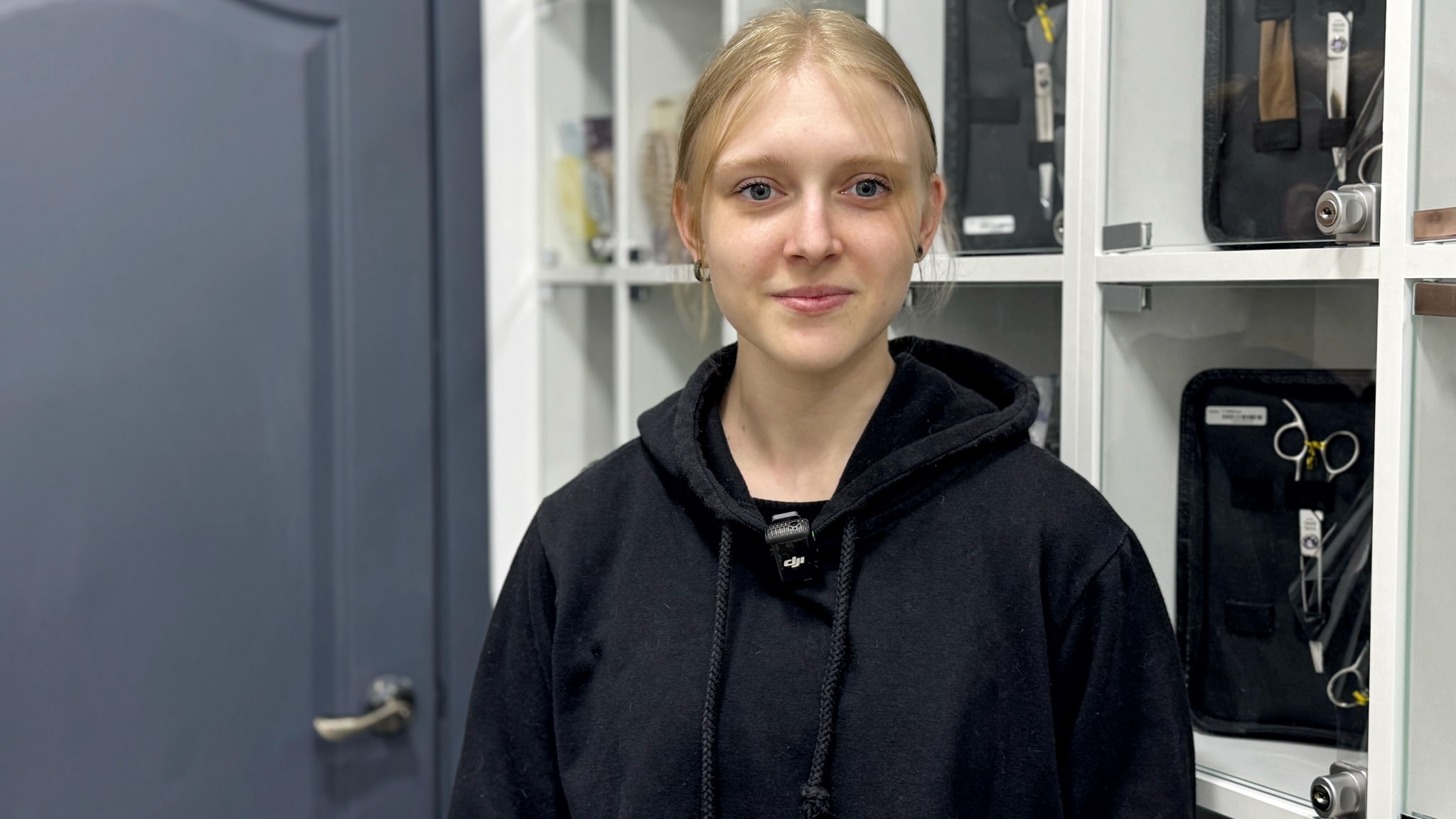 Дівчина з білим волоссям стоїть спиною до сірих дверей