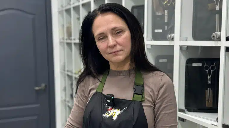 Жінка з чорним волоссям стоїть біля полиць з грумерськими ножицями