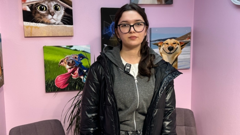 Дівчина в чорних окулярах та лаковій куртці має позаду себе картини з тваринами