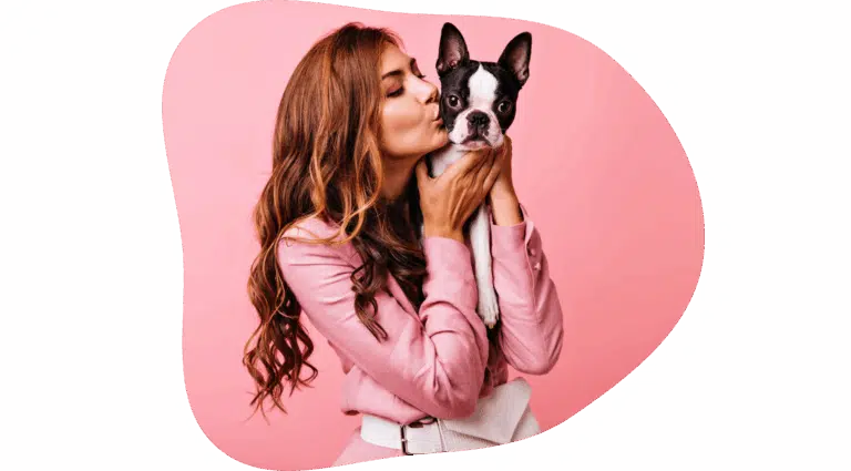 Дівчина в рожевому костюмі та з сумкою на поясі цілує в щічку маленького бостонського тер'єра