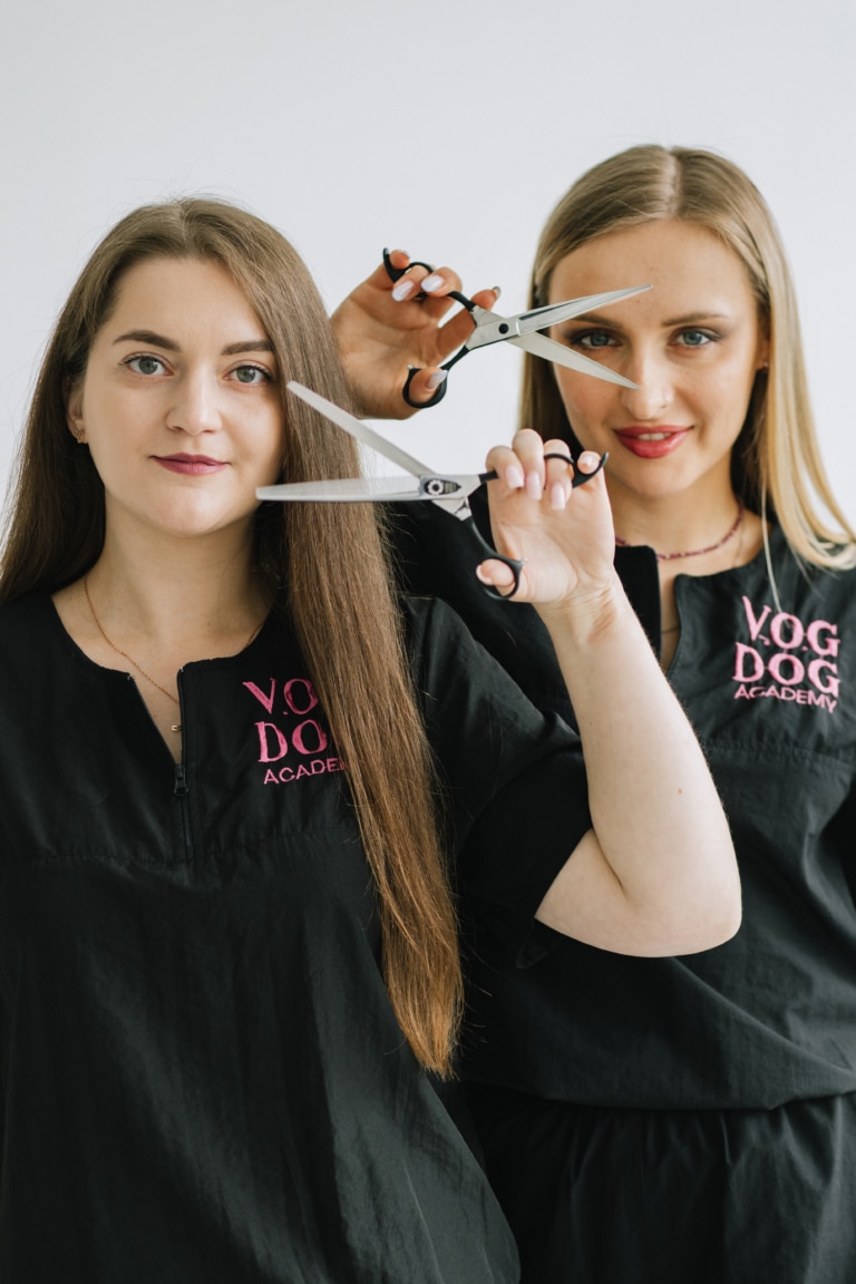 Дві дівчини тримають біля обличчя розкриті ножиці