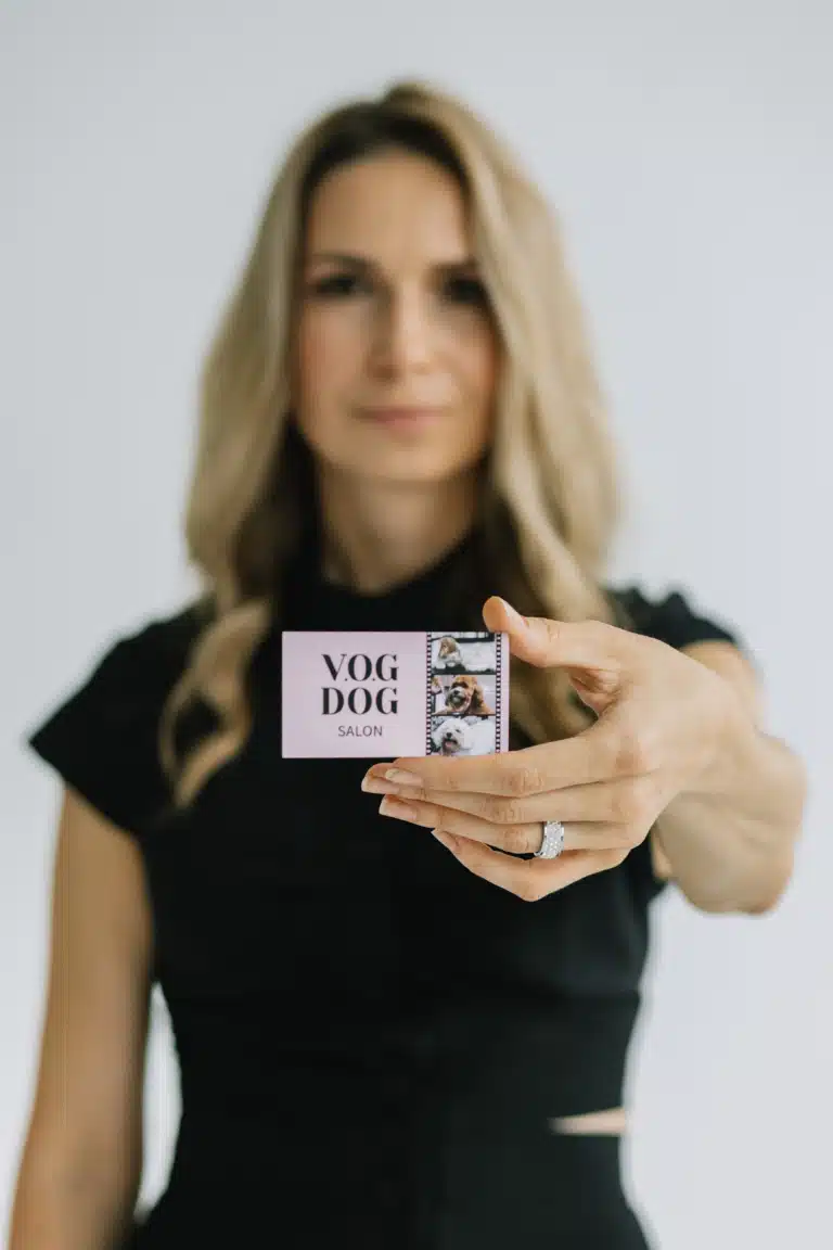 Дівчина в чорному одязі тримає перед собою рожеву візитівку зі стрічкою тварин