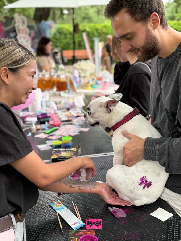 Чоловік тримає білого собаку з блискучим бантиком на попі на грумерському столі