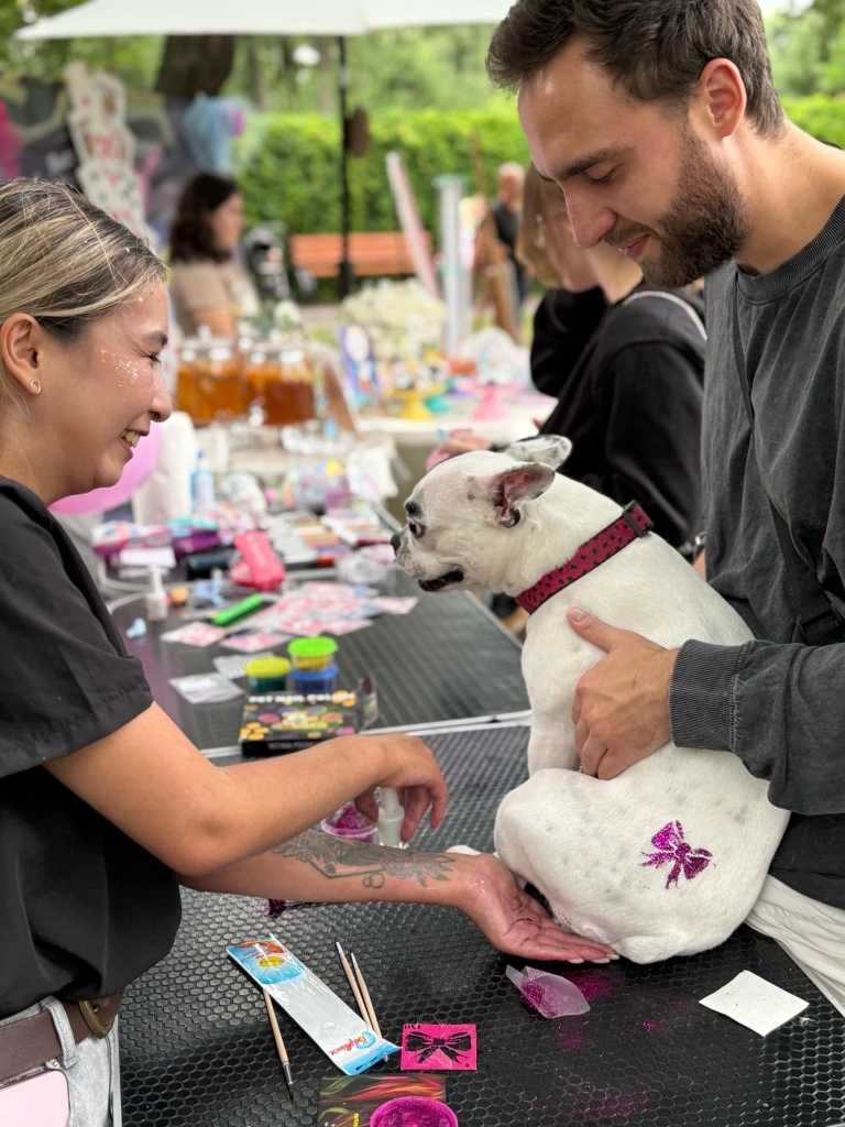 Чоловік тримає білого собаку з блискучим бантиком на попі на грумерському столі