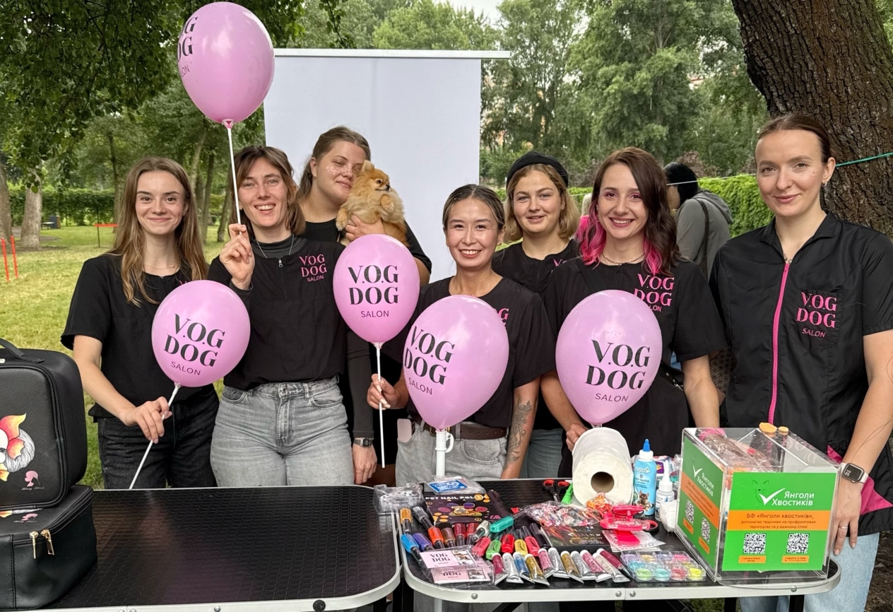 За двома грумерськими столами стоять грумери з рожевими кульками салону