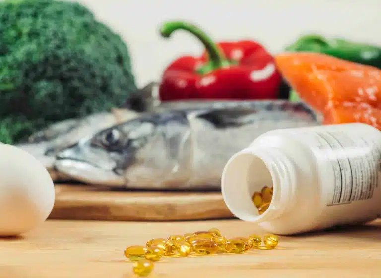 Біла баночка з прозорими пігулками поруч з овочами та сирою рибою