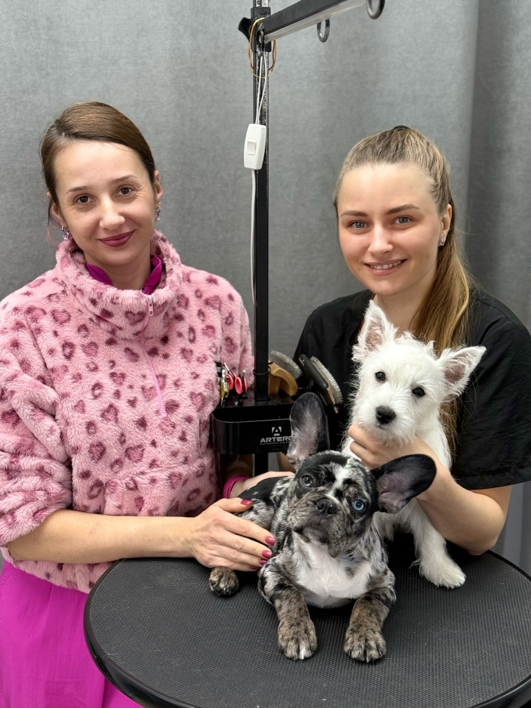 Дві дівчини стоять біля круглого столика, на якому знаходяться цуценята різних порід